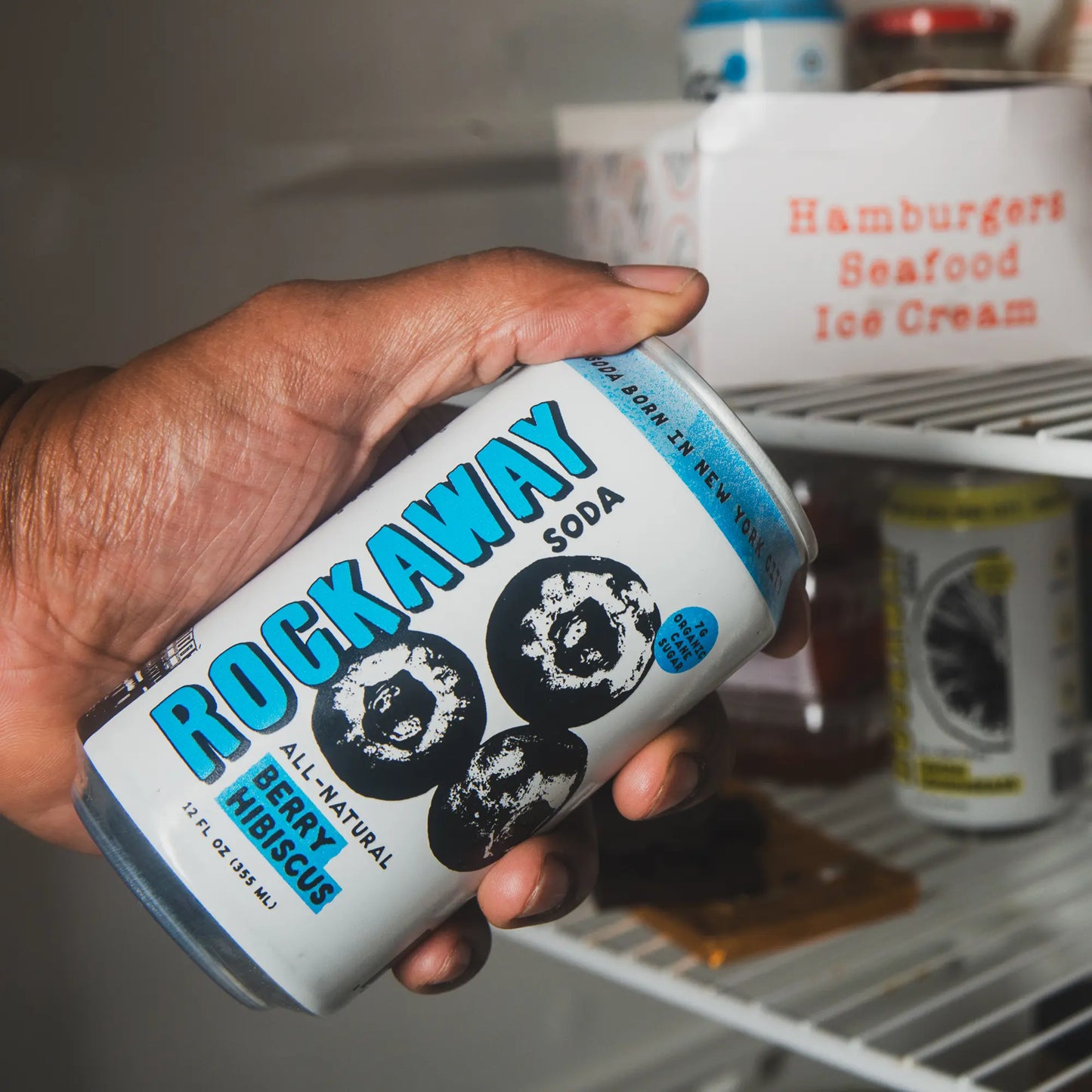 Rockaway Berry Hibiscus Soda Can in Hand. Background is a refrigerator.