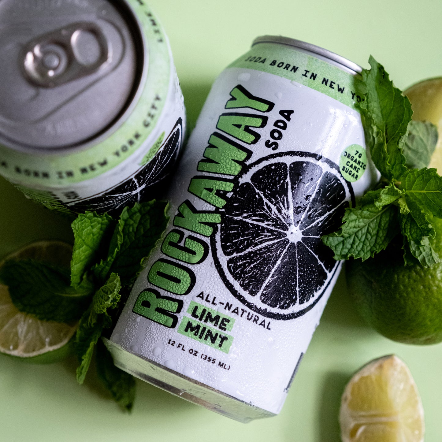 Two cans of Rockaway Lime Mint soda with lime slices and mint leaves on a green background